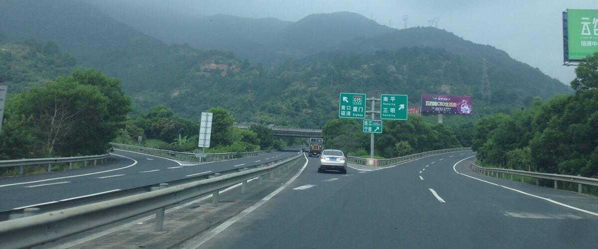 A highway with multiple lanes, green directional signs, and a mountainous landscape in the background.