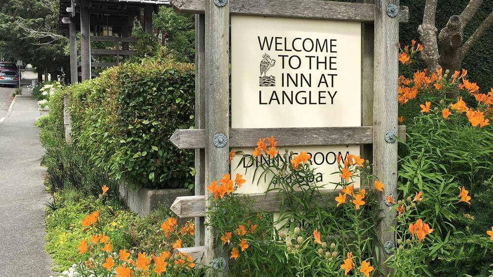 A wooden sign welcoming visitors to the Inn at Langley, surrounded by vibrant orange and white flowers.