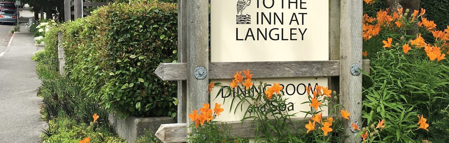 Un letrero de madera da la bienvenida a visitantes al Inn at Langley, rodeado de flores anaranjadas y blancas vibrantes.