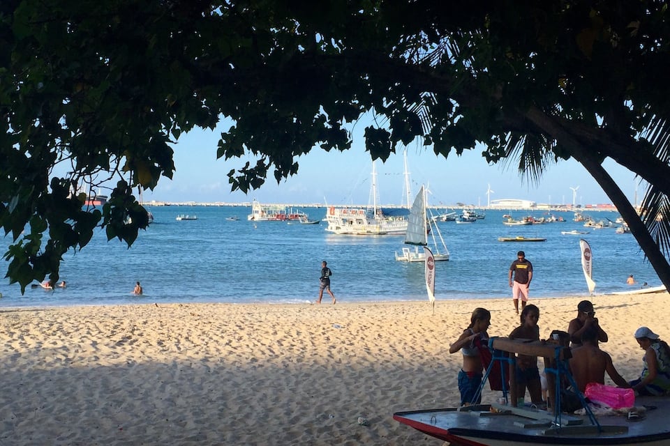 A beach with people, boats, and a sailboat named 'NETUNO' in the water.