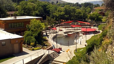 Um parque com um lago central, toldos vermelhos e vegetação ao redor.