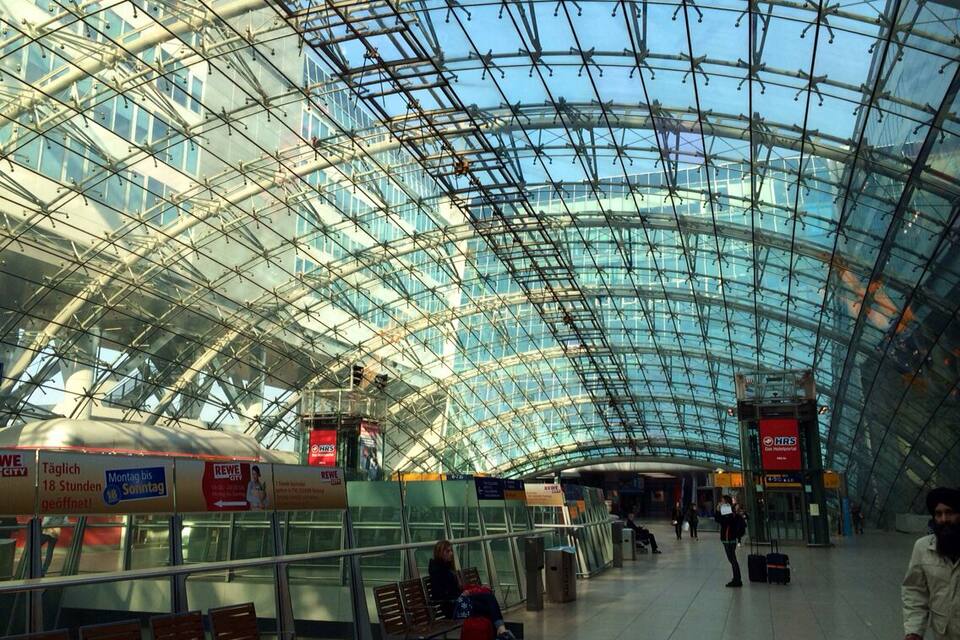 Ein moderner Bahnhof mit Glasdach, Bänken und Beschilderung.