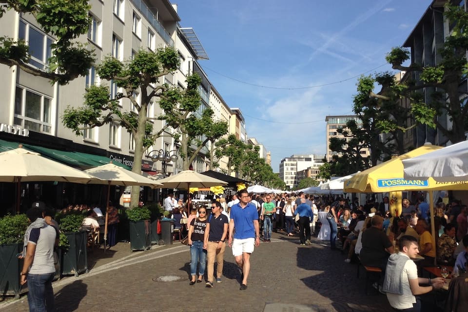 Un mercat a l'aire lliure animat, amb gent passejant i venedors sota ombrel·les.