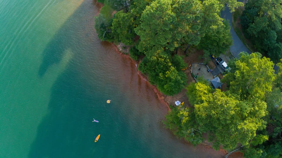 An aerial view of a coastal area with a beach, dense green trees, and a small dock with boats.