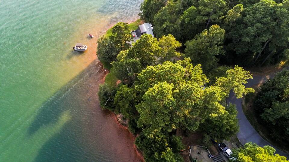 An aerial view of a lakeside property with dense trees, a dock, and a small building.