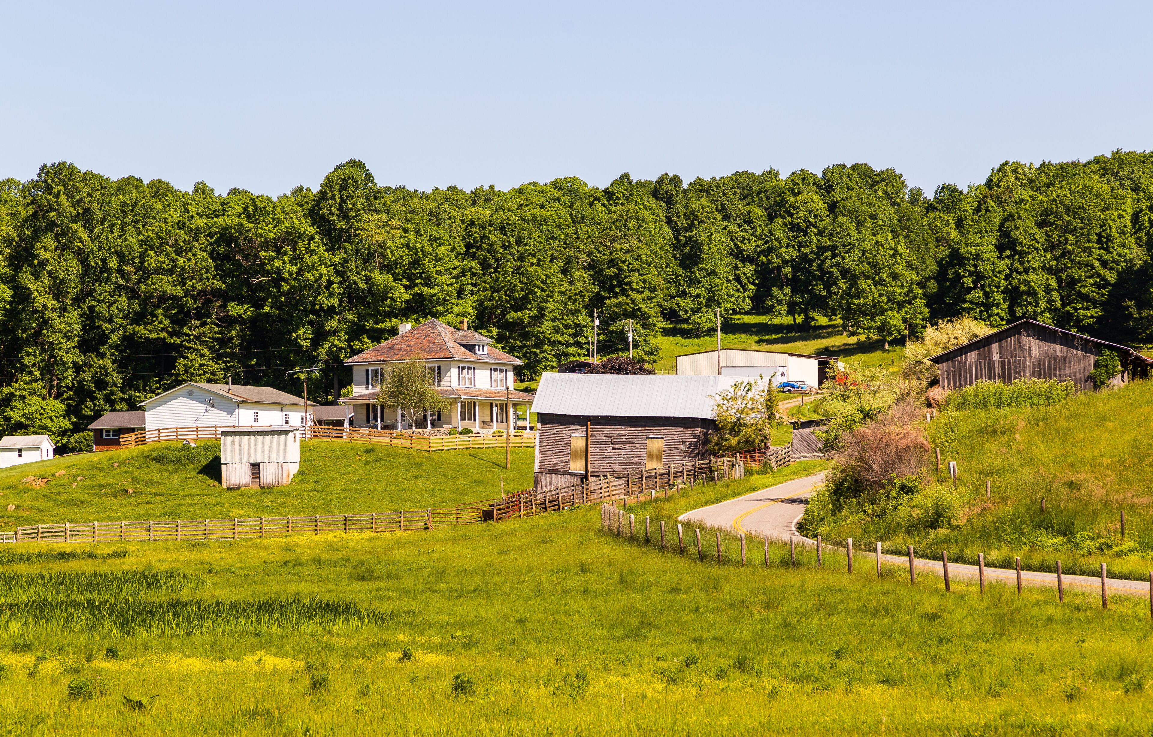 A rural landscape with a house, barns, and a forested hill.