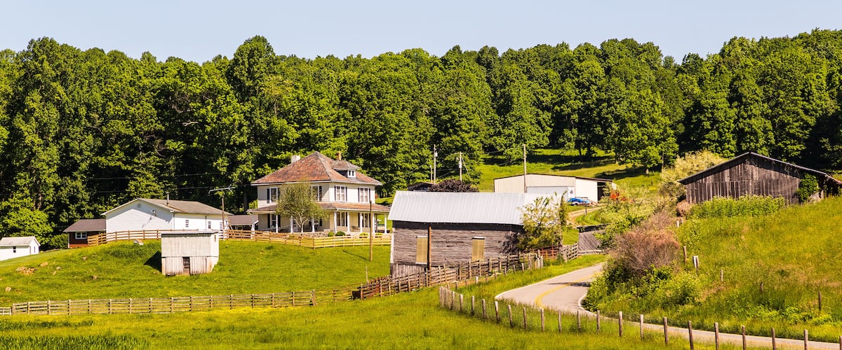 A rural landscape with a house, barns, and a forested hill.