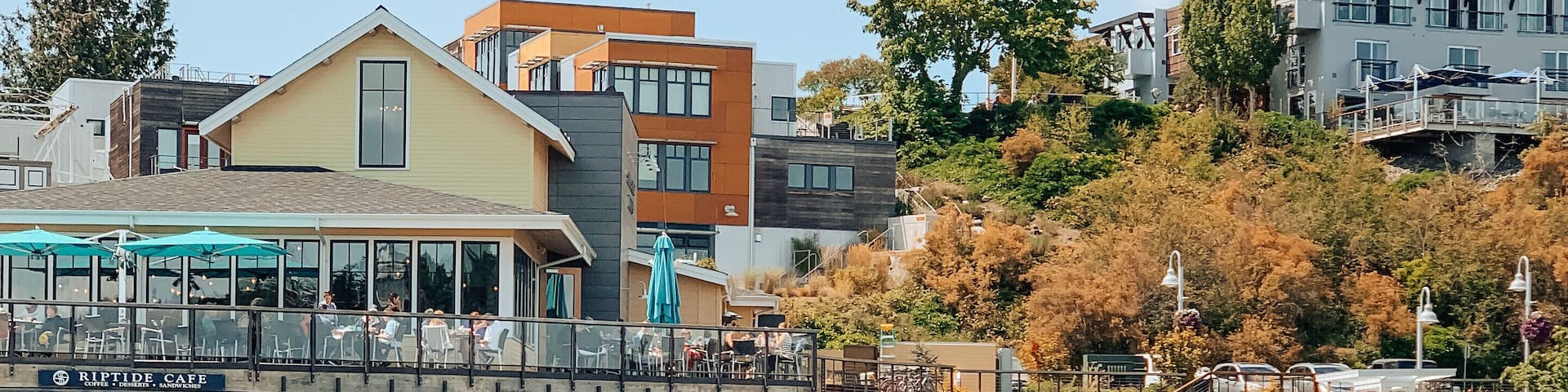 A marina with boats docked, a waterfront café, and buildings in the background.
