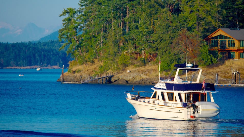 A boat on a calm body of water with a forested hillside and a house in the background.