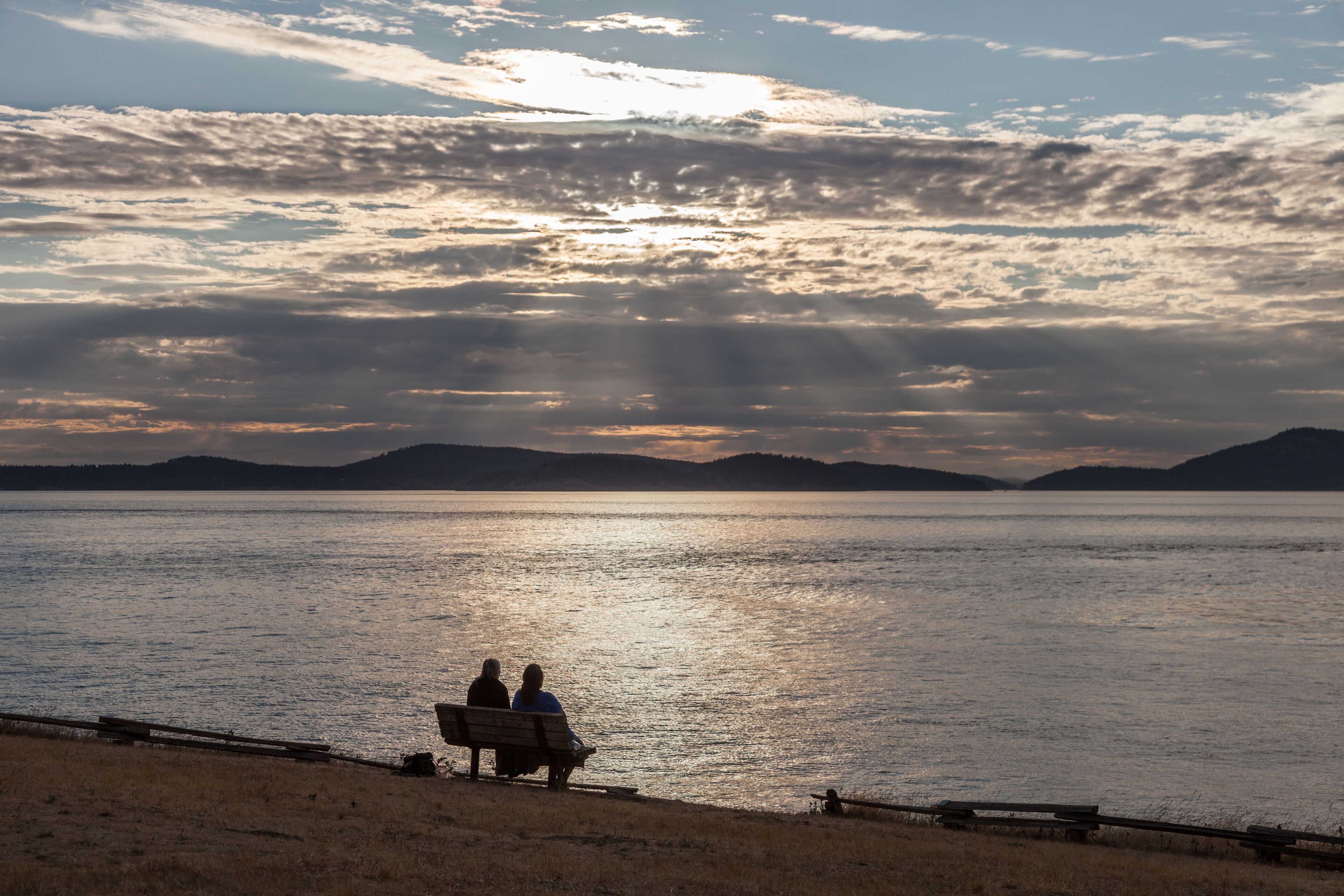 Un coucher de soleil sur un lac paisible, avec deux personnes assises sur un banc.