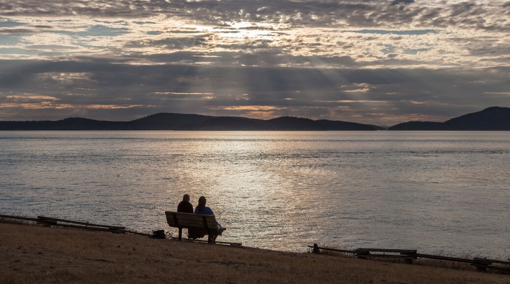 Un coucher de soleil sur un lac paisible, avec deux personnes assises sur un banc.