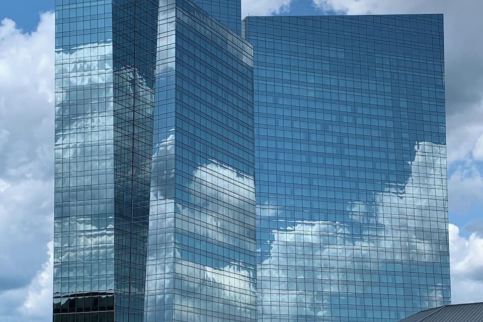 A modern glass skyscraper with a clear blue sky and clouds in the background.