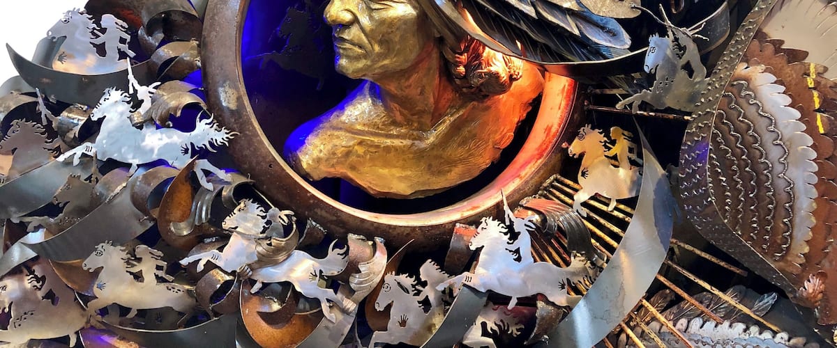 A sculpture with a central golden bust surrounded by metallic horse figures and intricate metalwork.