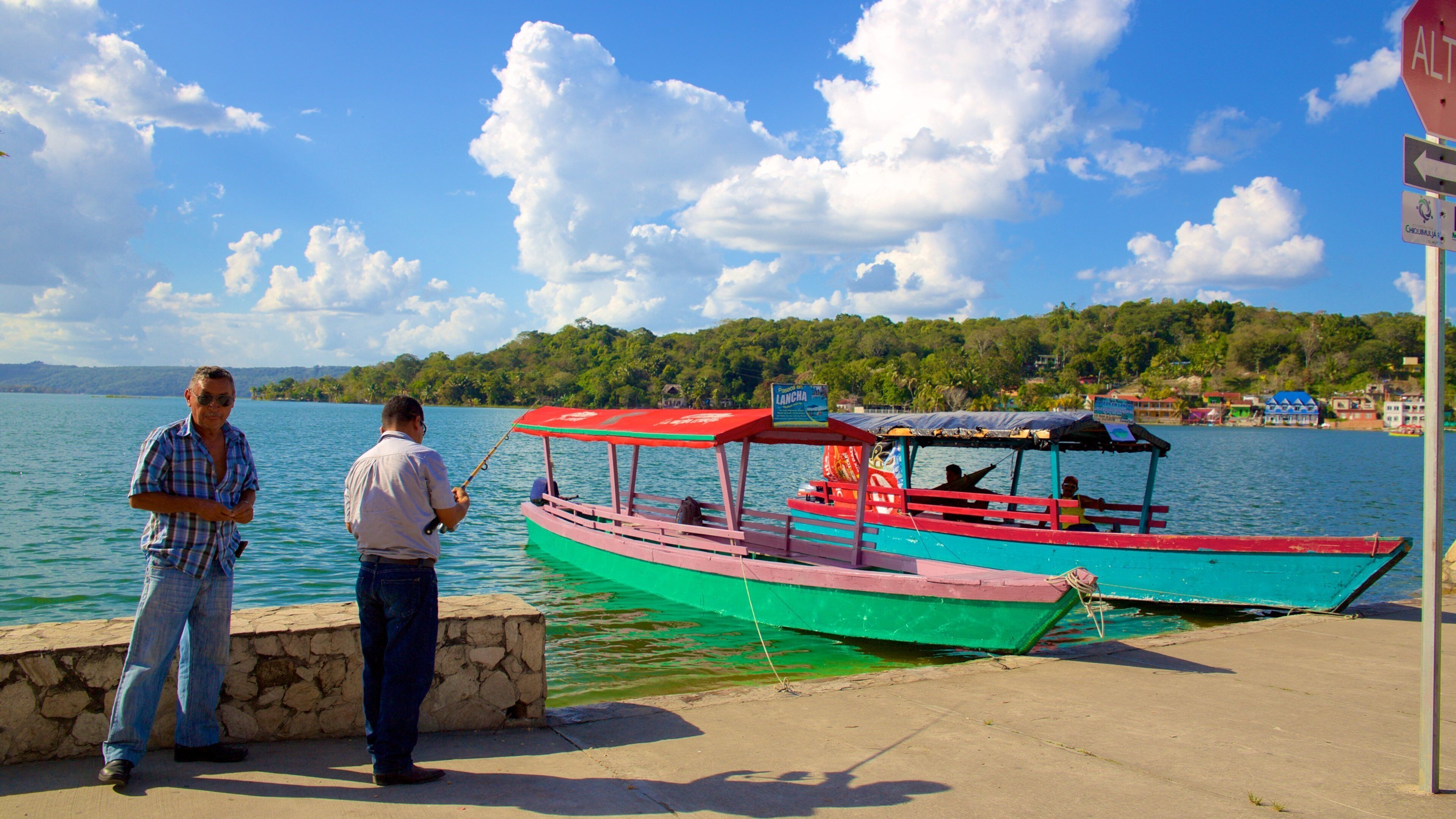 A man fishing by a dock with colorful boats in the background.
