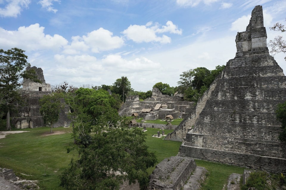 Ancient Mayan ruins with large stone structures and a grassy area.