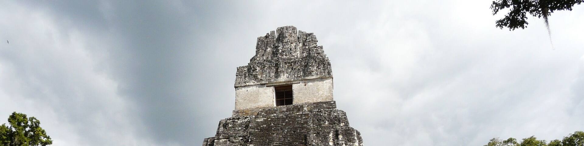 A large pyramid structure with a staircase leading to the top, surrounded by lush greenery and trees.