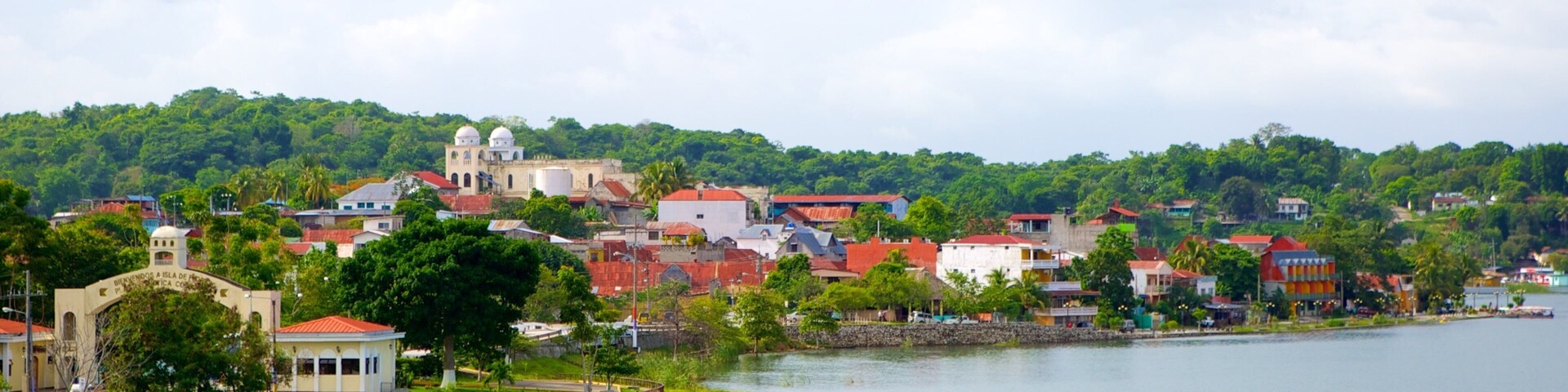 Un pueblo junto al lago con edificios de tejados rojos, una iglesia y abundante vegetación.