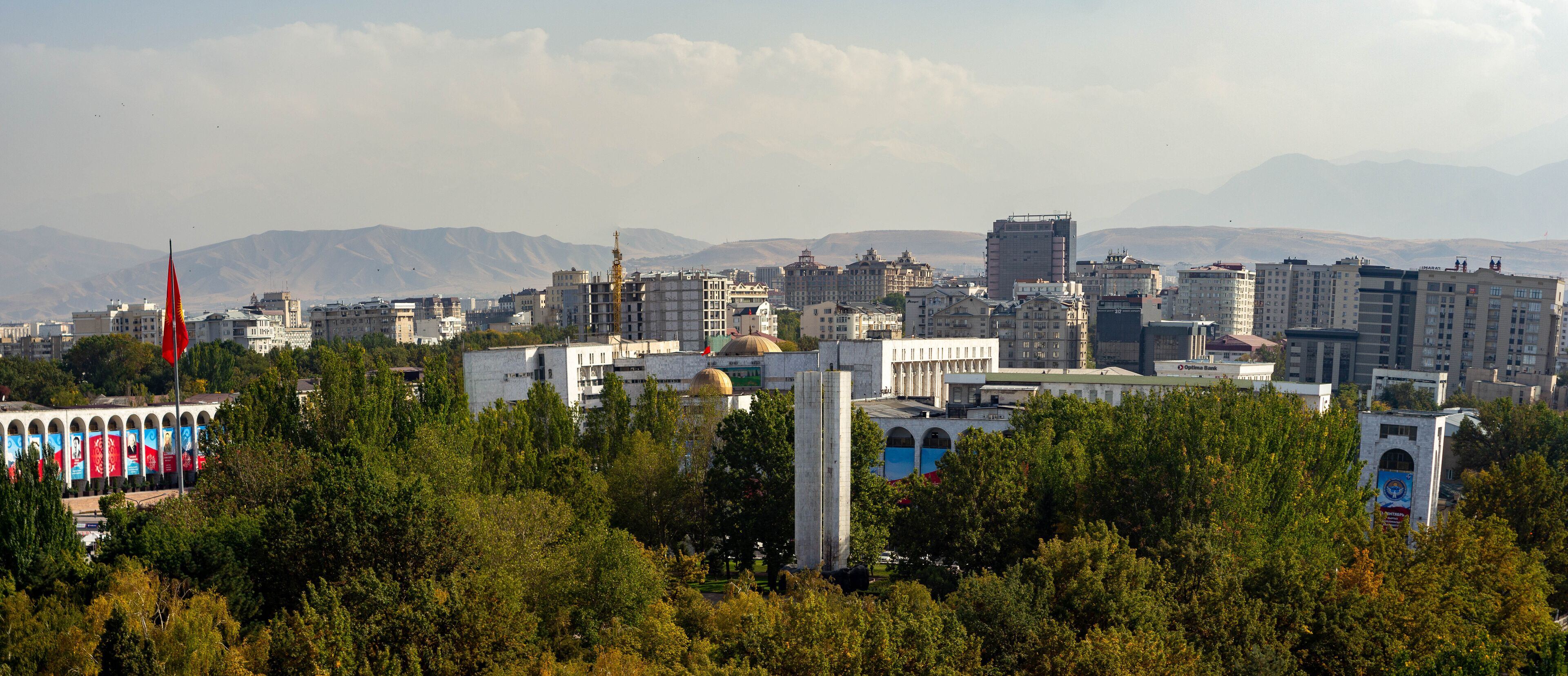 A cityscape with a prominent mosque, a tall minaret, and a backdrop of mountains.