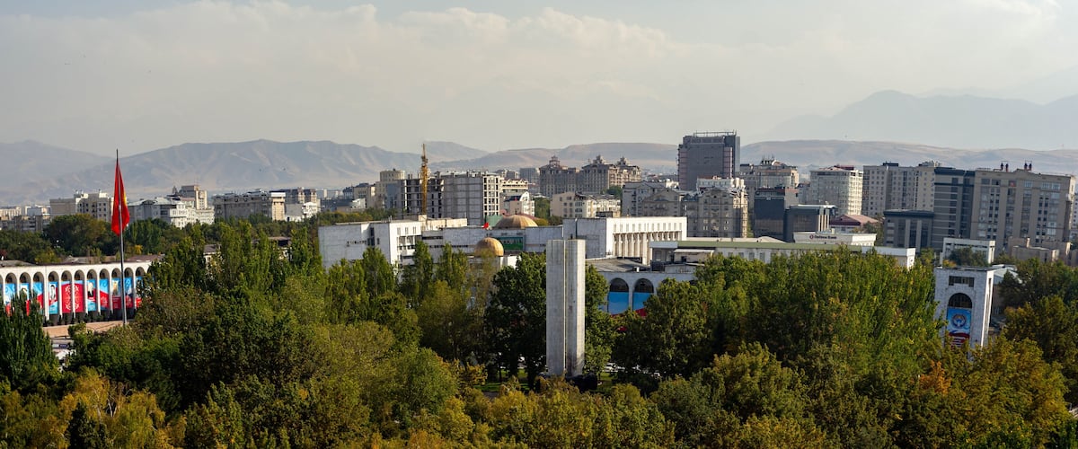 A cityscape with a prominent mosque, a tall minaret, and a backdrop of mountains.