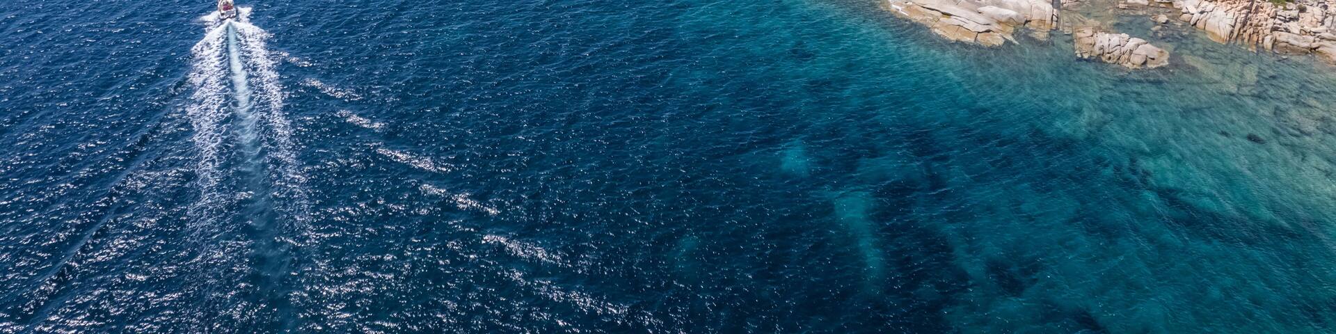 Aerial view of a small sailing boat navigating along the coastline, Figari, Corse, France.