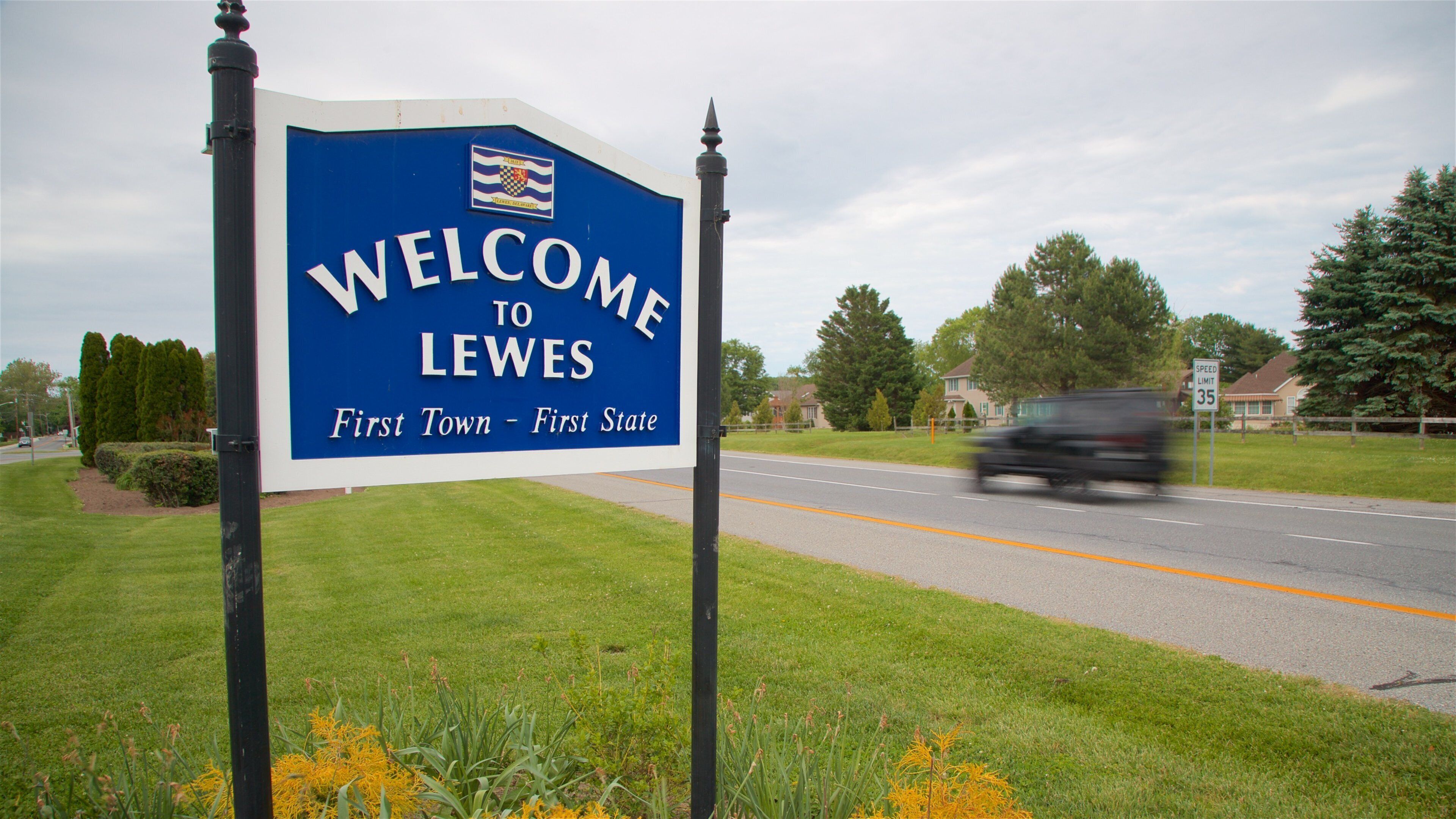 A welcome sign for Lewes, a town sign, a road, and a speed limit sign.