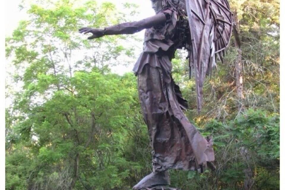 A statue of a figure with outstretched arms and a spherical base, set in a park with trees in the background.