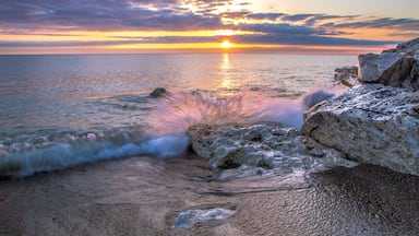 Waves Crashing On Beach. Wave crashing over a rocky coast with sunrise colors reflecting on the waters of Lake Huron In Lexington, Michigan.