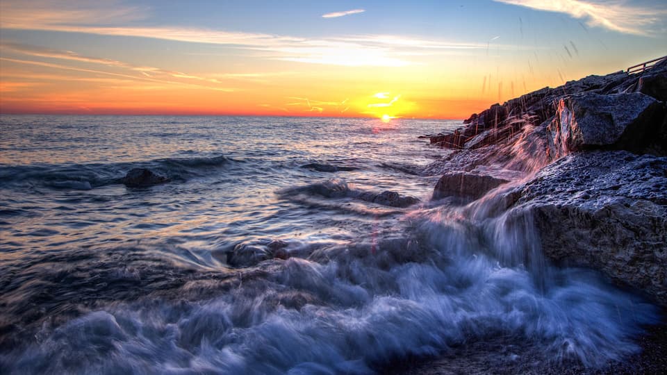 Beautiful Sunrise Beach Background. Waves crash onto the rocks of a Lake Huron beach with a sunrise horizon in the background. Lexington, Michigan.
