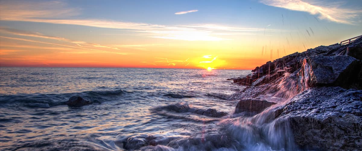 Beautiful Sunrise Beach Background. Waves crash onto the rocks of a Lake Huron beach with a sunrise horizon in the background. Lexington, Michigan.