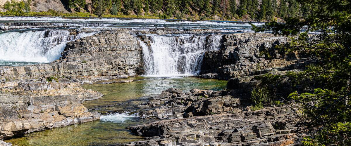 A multi-tiered waterfall cascading over rocky terrain with clear water at the base.