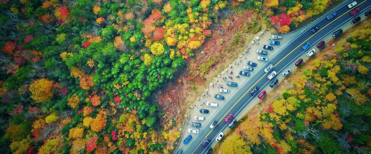 An aerial view of a highway cutting through a forest with autumn foliage.