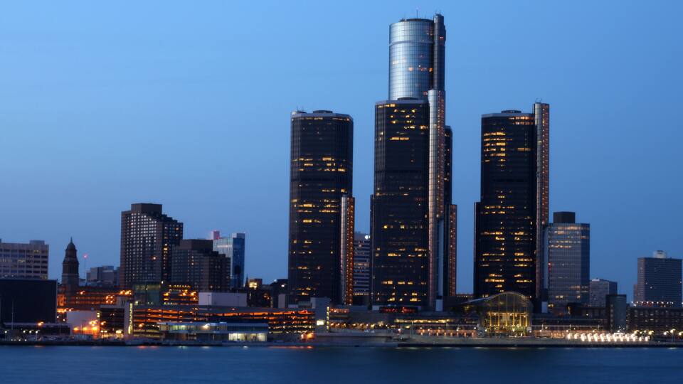 A city skyline with several high-rise buildings, a body of water in the foreground, and a distinctive curved building in the center.