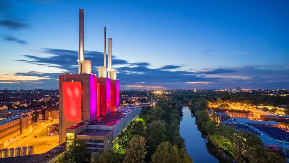 A large industrial complex with tall chimneys, a river, and surrounding greenery.