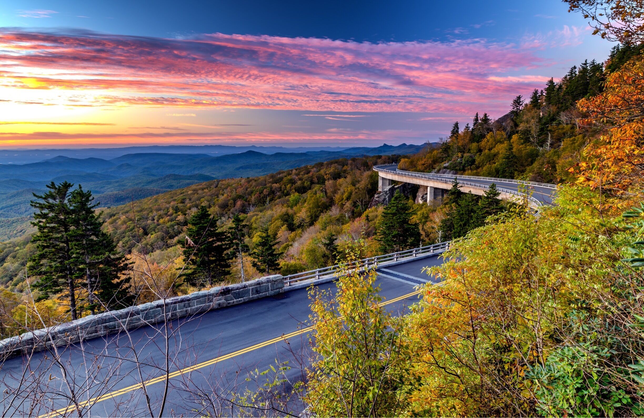 A winding road through a mountainous landscape with autumn foliage.