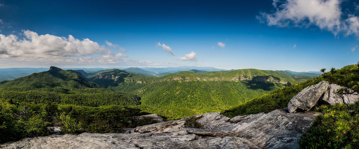 A mountainous landscape with dense green forests and rocky outcrops under a clear blue sky.