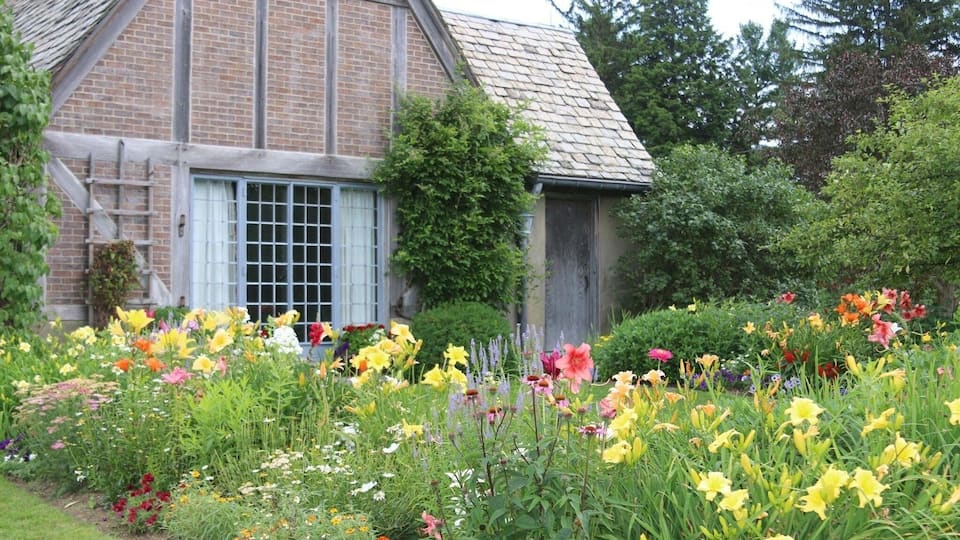 A brick house with a sloped roof and a garden full of colorful flowers.