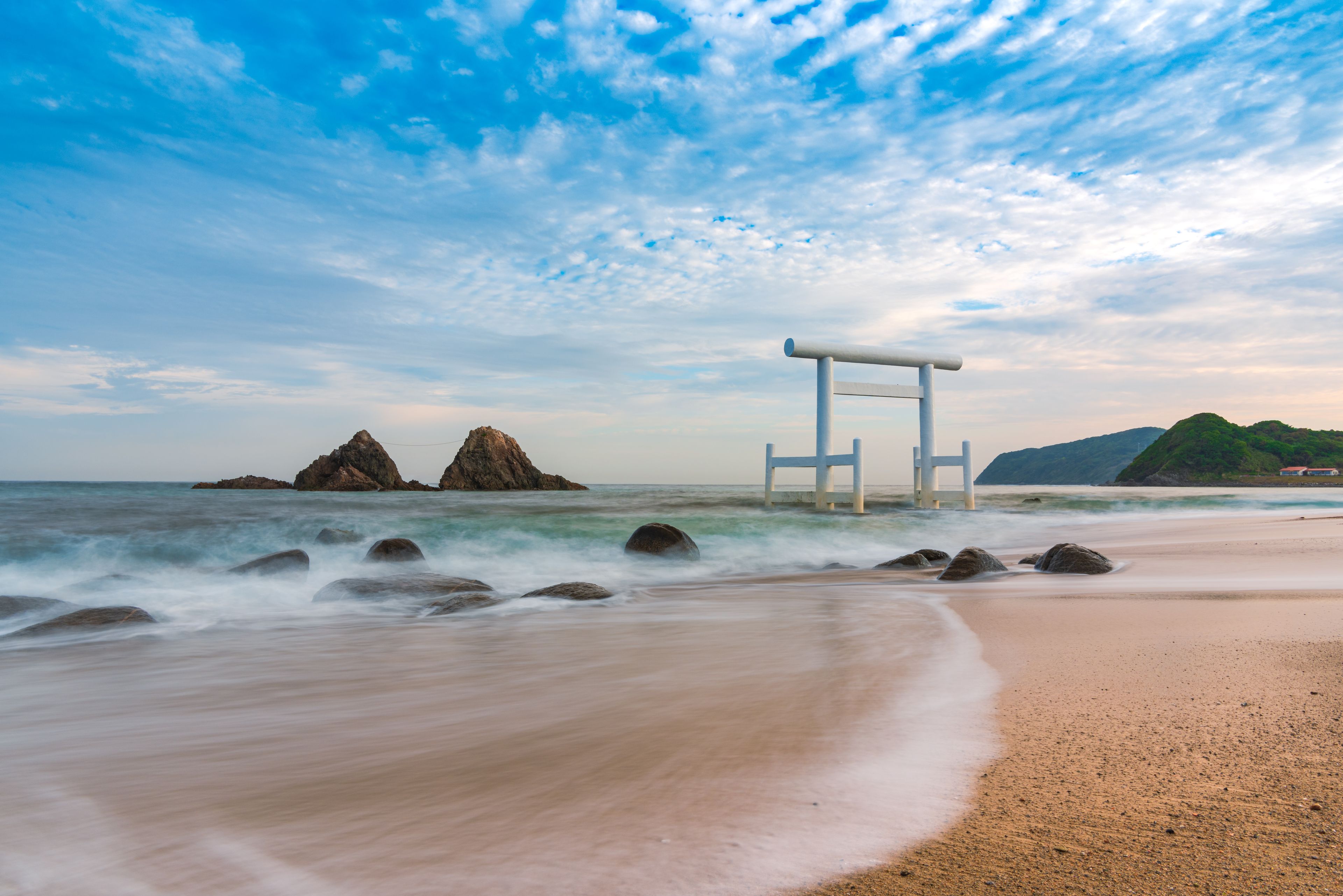 Una playa con una estructura blanca, olas y afloramientos rocosos.