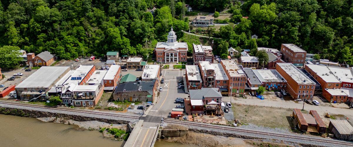 An aerial view of a town with a prominent red-brick courthouse, a railway crossing, and dense forest in the background.