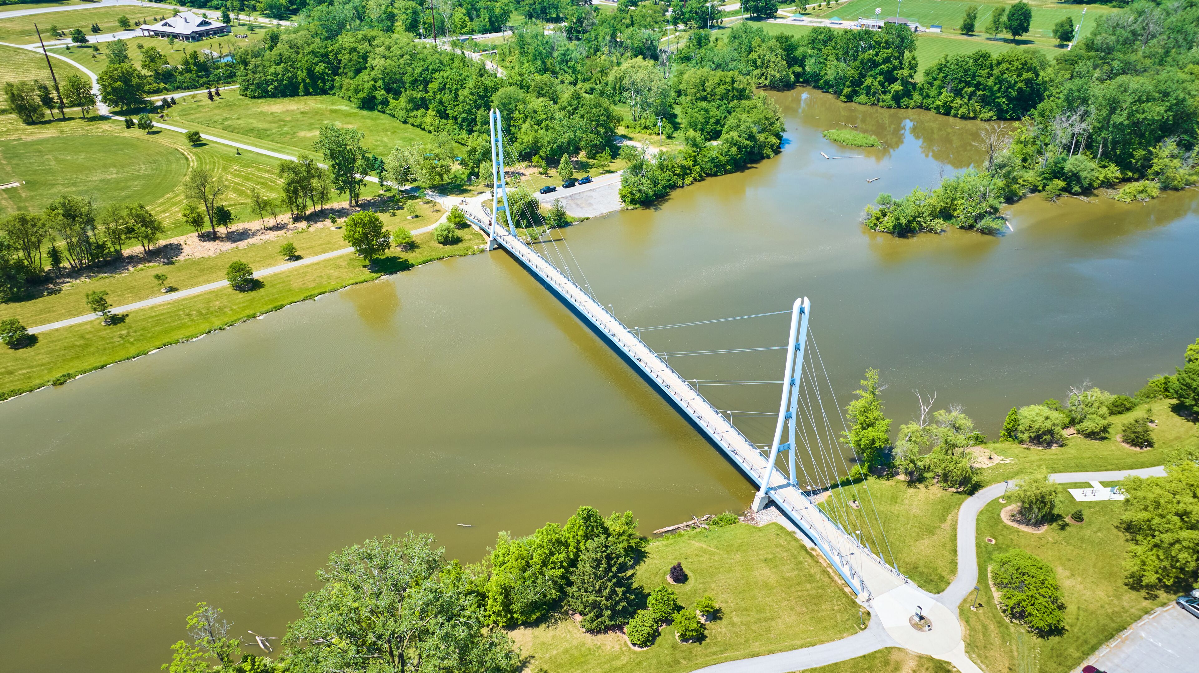 Un puente colgante cruza un río, rodeado de abundante vegetación y un pequeño edificio.