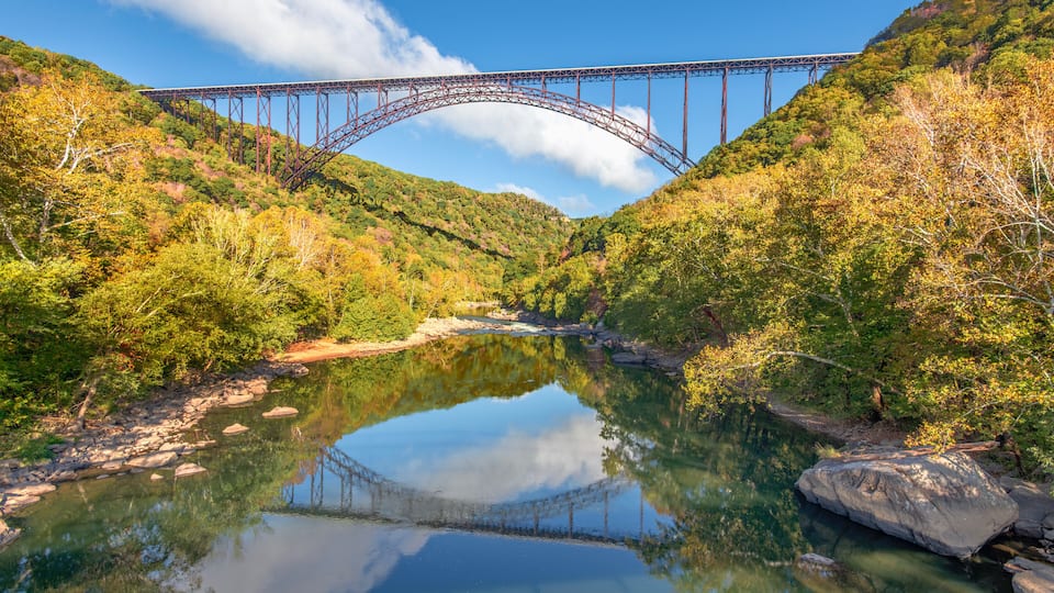 A steel bridge spanning a river, surrounded by autumn foliage and hills.