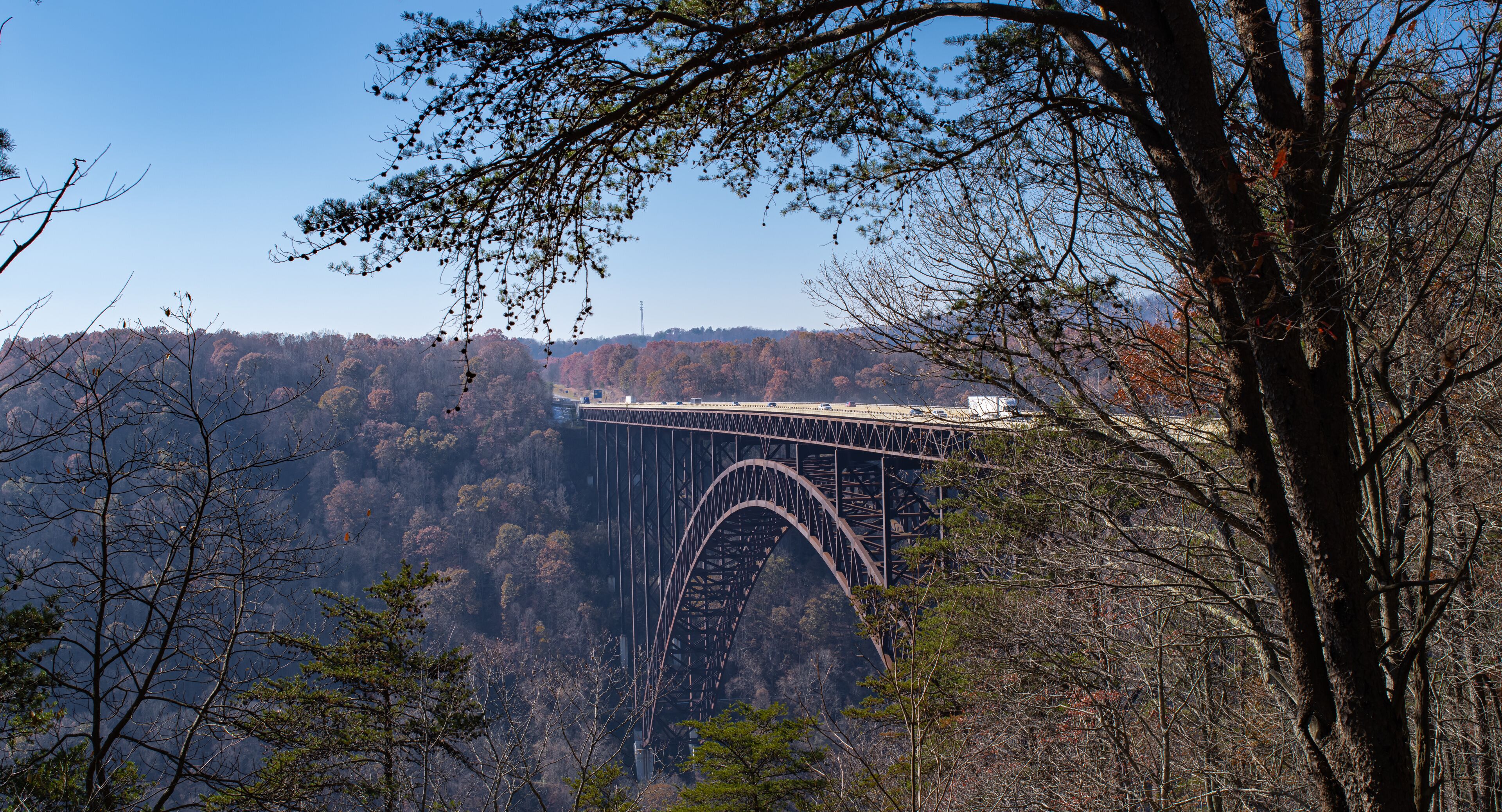 A steel arch bridge over a forested valley with a clear blue sky.