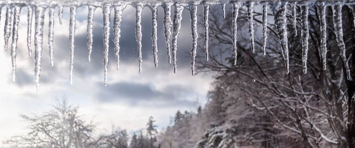 The white winter wonderland scenery in Londonderry, Vermont with snow covered trees, icicles and blue cloudy sky in the background on a cold day. Selective focus.