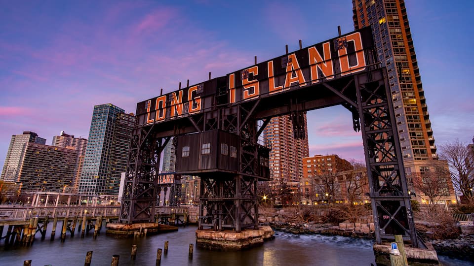 A bridge with 'LONG ISLAND' written on it, surrounded by city buildings and a river.