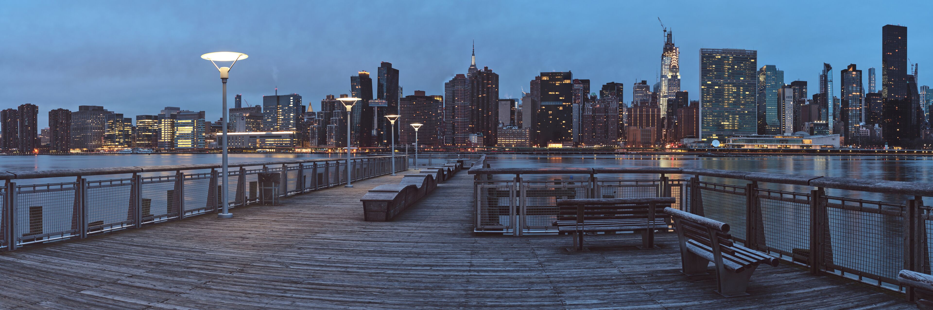 A waterfront promenade with benches and a city skyline in the background.
