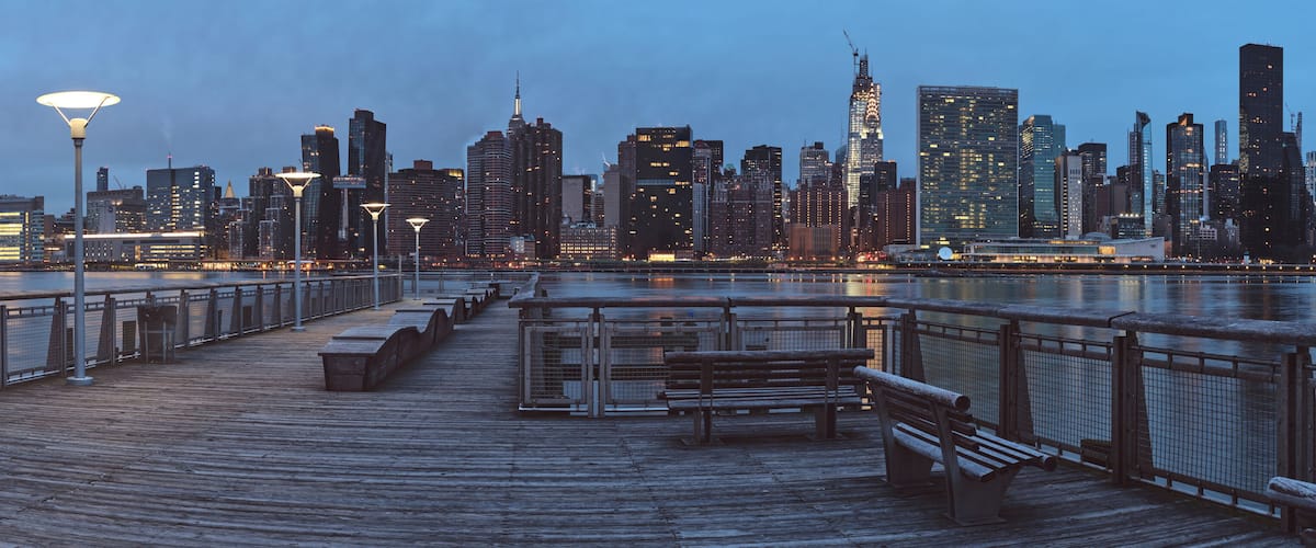 A waterfront promenade with benches and a city skyline in the background.
