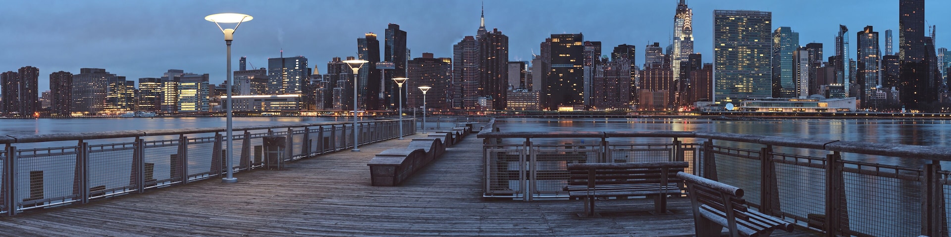 A waterfront promenade with benches and a city skyline in the background.