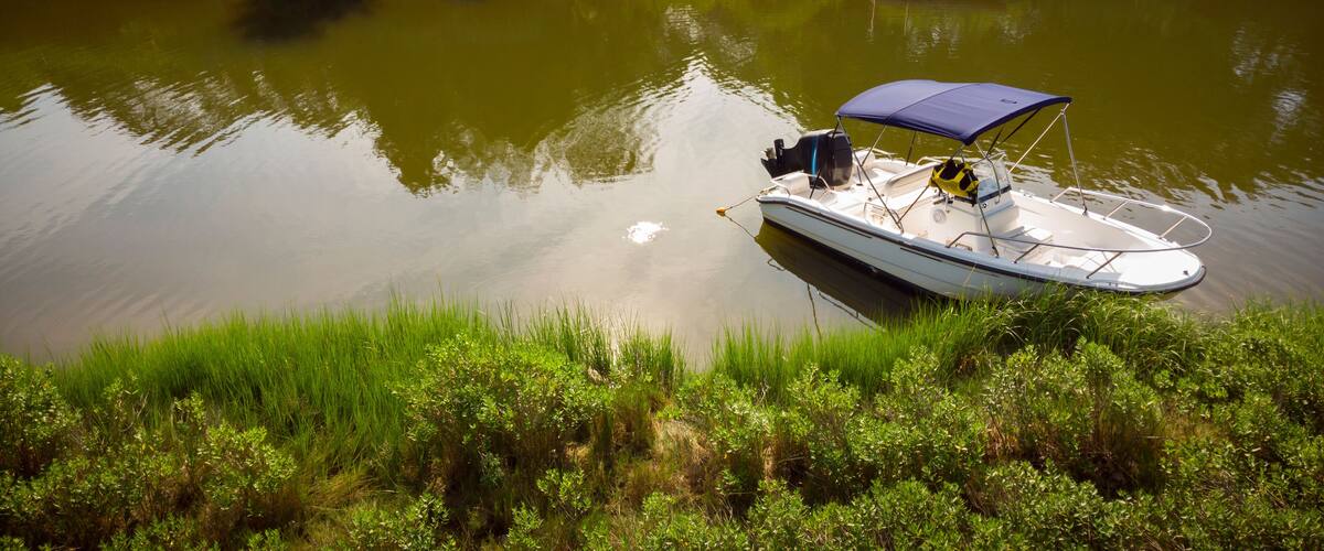 A small boat with a canopy anchored near a dock.