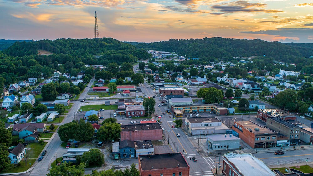 A town with a prominent tower, a mix of residential and commercial buildings, and a hilly backdrop.