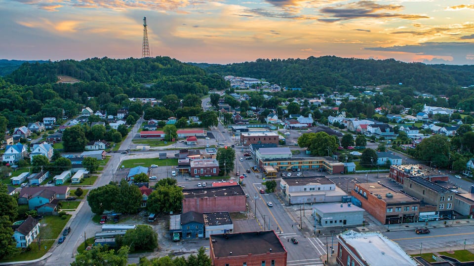 A town with a prominent tower, a mix of residential and commercial buildings, and a hilly backdrop.