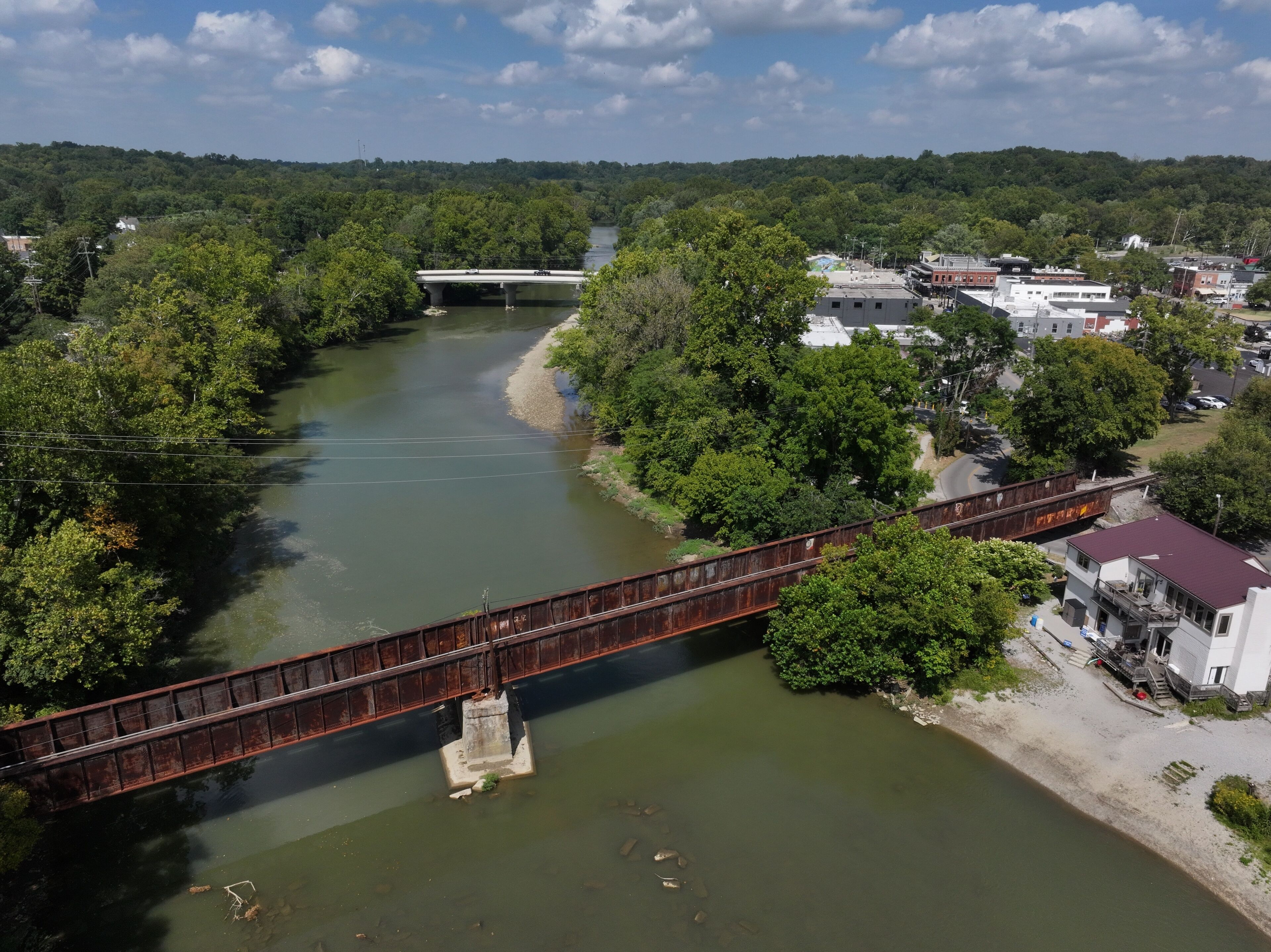 Aerial view of the Little Miami River winding through verdant trees, crossed by a rusty bridge near Loveland, Ohio, United States.